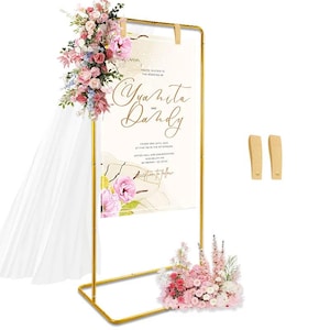 May include: A gold metal wedding sign with a floral arrangement of pink, red, and white flowers. The sign displays the names "Gyanita and Dandy" and wedding details. Two wooden clips are included.
