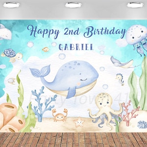 May include: A blue and turquoise watercolor-style backdrop featuring an underwater scene with a whale, octopus, and other sea creatures. The text "Happy 2nd Birthday GABRIEL" is displayed in blue script.
