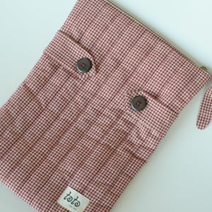 May include: A rectangular, quilted pouch in a red and white gingham pattern. The pouch has two large brown buttons, a zipper closure, and a small fabric tag with the word "toto". The pouch has a small fabric loop on the side.