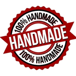 Op de afbeelding: Een rode en zwarte ronde stempel met de tekst "100% HANDMADE" rond de rand en "HANDMADE" in witte letters op een rood lint.