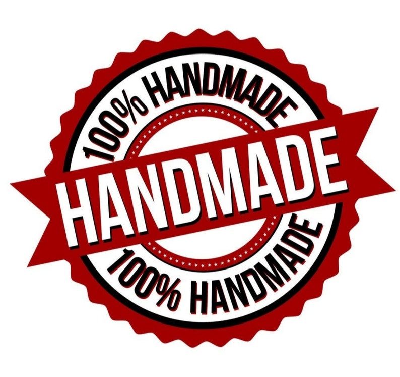 Op de afbeelding: Een rode en zwarte ronde stempel met de tekst "100% HANDMADE" rond de rand en "HANDMADE" in witte letters op een rood lint.