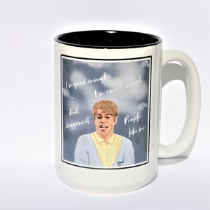 以下が含まれることがあります： 黒縁と取っ手が付いた白いセラミックマグカップ。マグカップには、金髪の青いセーターを着た人物のグラフィックが描かれています。マグカップのテキストは「I'm good enough. I'm smart enough. And. People like me.」です。