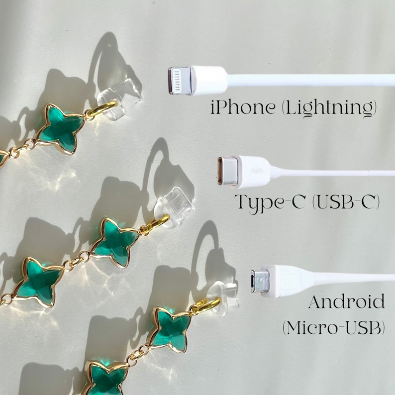 May include: A close-up of three white charging cables with different connector types: iPhone (Lightning), Type-C (USB-C), and Android (Micro-USB).  Green clover-shaped earrings with gold accents are in the foreground.