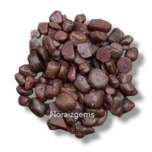 Könnte beinhalten: Ein Haufen kleiner, rauer, rotbrauner Edelsteine. Die Steine sind in verschiedenen Formen und Größen, einige haben einen polierteren Look. Die Steine liegen auf einem weißen Hintergrund.