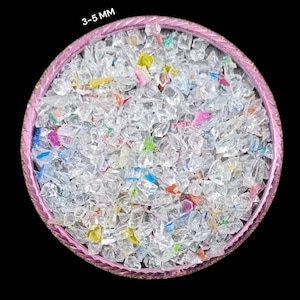 Può includere: Una vista ravvicinata di una ciotola rosa piena di pezzi di vetro trasparenti e traslucidi, che vanno da 3 a 5 millimetri di dimensione. I pezzi di vetro sono principalmente trasparenti, con alcuni piccoli pezzi di vetro colorato mescolati.