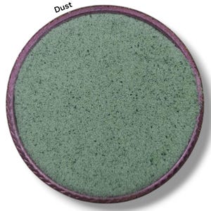 Pode incluir: Um compacto de sombra de olhos redondo e verde com uma superfície texturizada. O compacto tem uma borda rosa escura e a palavra "Dust" está impressa no topo. Um produto de beleza.