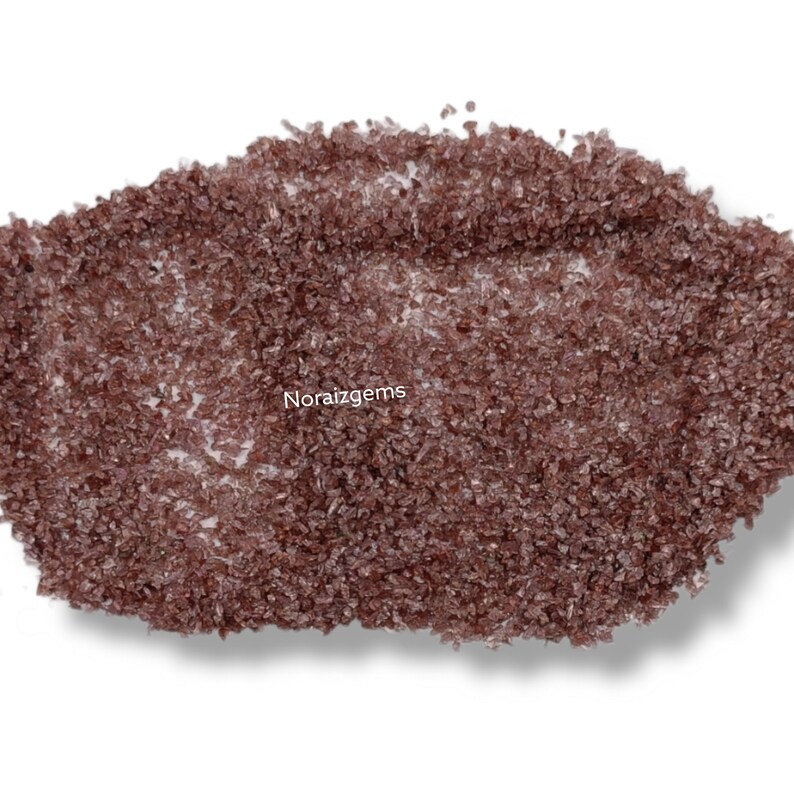 K&ouml;nnte beinhalten: Nahaufnahme eines Haufens kleiner, rotbrauner Kristalle. Die Kristalle sind unregelm&auml;&szlig;ig geformt und haben einen leicht metallischen Glanz. Die Kristalle sind auf einem wei&szlig;en Hintergrund verstreut.