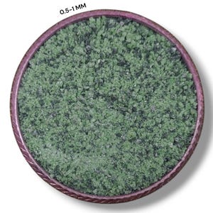 May include: A close-up view of a circular container filled with small, irregularly shaped green and dark gray stones. The container has a dark pink rim. The text "0.5-1 MM" is at the top of the image.