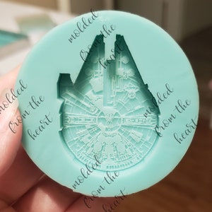 May include: A light blue silicone mold with the text "molded from the heart" repeated around the edge. The mold is shaped like the Millennium Falcon spaceship from Star Wars.