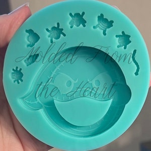 May include: A teal silicone mold with a smiling face and several small bug shapes around the edge. The mold says "Molded From the Heart".