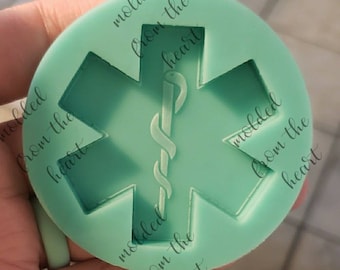May include: A green silicone mold shaped like a medical star of life with a snake wrapped around a rod in the center. The mold has the text "molded from the heart" repeated around the edge.