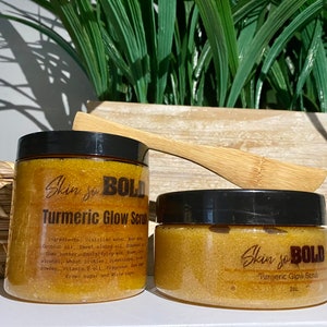 May include: Two jars of turmeric glow scrub with a black lid and a wooden scoop. The jars are labelled "Skin so BOLD Turmeric Glow Scrub". The scrub is a bright yellow colour.
