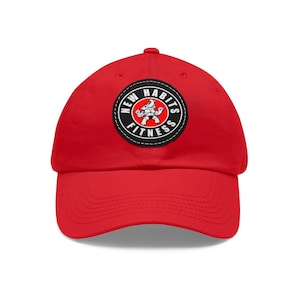 May include: A bright red baseball cap featuring a circular black and white patch on the front. The patch displays the text NEW HABITS FITNESS in a bold white font surrounding a central graphic of a muscular cartoon rhinoceros in a red circle.