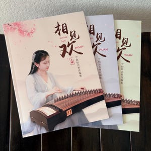 May include: Three books with Chinese text and images of a woman playing a guzheng, a traditional Chinese instrument. The covers are in pastel colors, with the main book featuring a woman in a white dress and cherry blossoms.