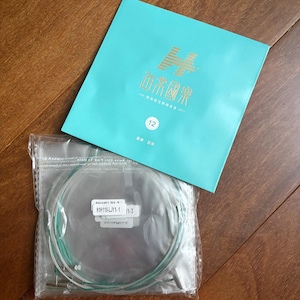 Peut inclure: Un livret turquoise avec du texte doré et le chiffre 12 est à côté d'un sac en plastique transparent contenant un câble circulaire teinté de vert. Le sac a une étiquette blanche avec du texte noir.