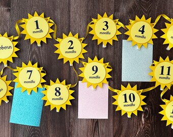 May include: A yellow sun-shaped banner with black numbers and text, "newborn", "1 month", "2 months", "3 months", "4 months", "5 months", "6 months", "7 months", "8 months", "9 months", "10 months", "11 months", and "12 months".
