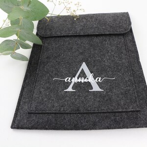 May include: A gray felt laptop sleeve with a white embroidered letter A and the name "annika" in cursive.