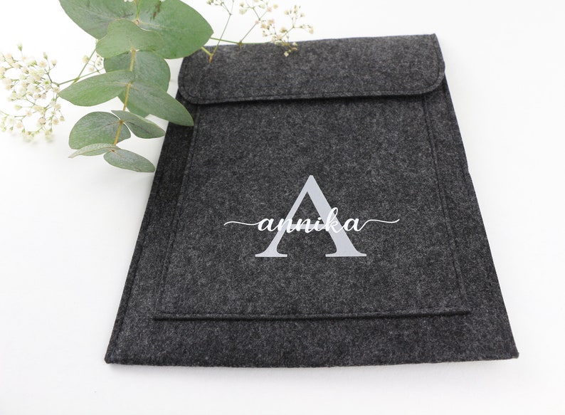 May include: A gray felt laptop sleeve with a white embroidered letter A and the name "annika" in cursive.