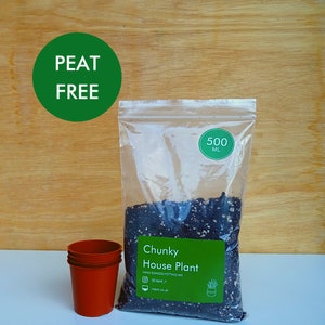 May include: A clear plastic bag of chunky house plant potting mix, labelled "Peat Free" and containing 500 ml. Three small, terracotta-coloured plant pots are visible. The background is a light wood grain.
