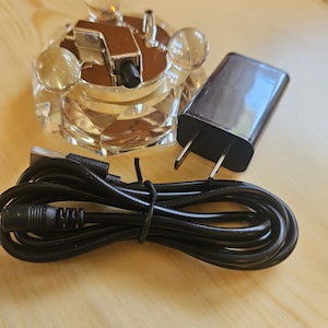 May include: A black power adapter with a cord and a clear crystal base with a silver metal top. The base has four clear crystal balls on the top.
