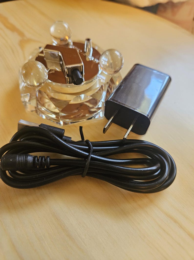 May include: A black power adapter with a cord and a clear crystal base with a silver metal top. The base has four clear crystal balls on the top.