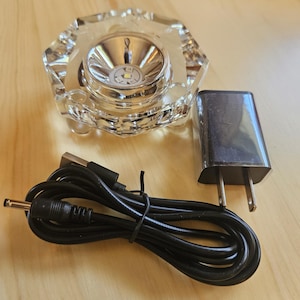 May include: A clear glass crystal base with a small LED light in the center. The base is connected to a black power cord and a white power adapter with a US plug.