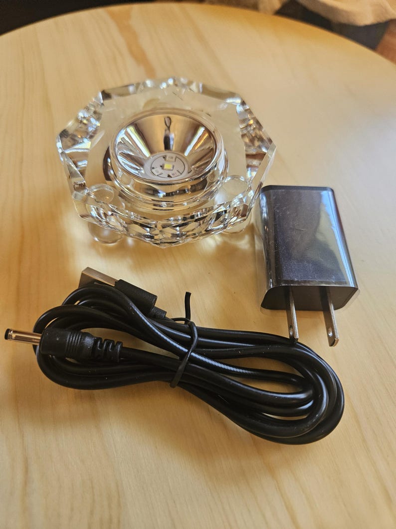 May include: A clear glass crystal base with a small LED light in the center. The base is connected to a black power cord and a white power adapter with a US plug.