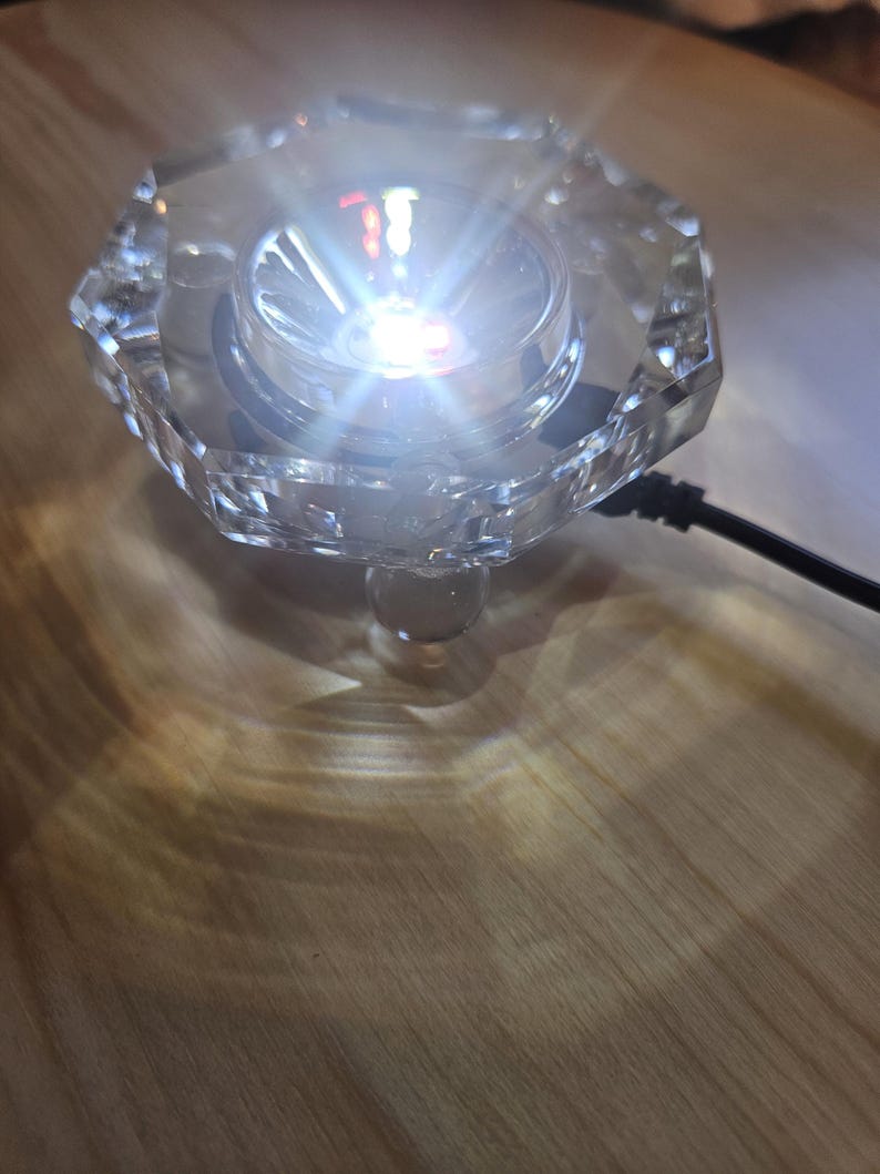 May include: A clear crystal base with a small, bright white LED light in the center. The base has a faceted design and a clear glass stem.