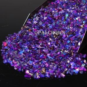 Könnte beinhalten: Nahaufnahme eines Haufens zerdrückter Opal-Edelsteine in Lila-, Blau- und Rosatönen. Die Edelsteine ​​befinden sich in einer Metallschaufel, mit dem Text "OPALCROWN" sichtbar. Die Edelsteine ​​haben eine reflektierende, irisierende Qualität.