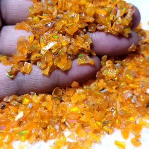 Könnte beinhalten: Eine Ansammlung kleiner, unregelmäßiger, getrommelter oranger Opal-Edelsteinsplitter. Die durchscheinenden Steine weisen leuchtende Orangetöne mit verstreuten grünen und gelben Irisierungen auf den facettierten, polierten Oberflächen auf.
