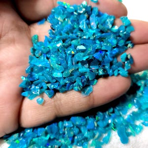 Könnte beinhalten: Eine Ansammlung kleiner, unregelmäßiger, leuchtend blauer Opal-Splitter mit irisierenden grünen und gelben Reflexen. Die Steine sind durchscheinend und haben eine polierte, glänzende Textur mit einer lebendigen, gesättigten Farbe.