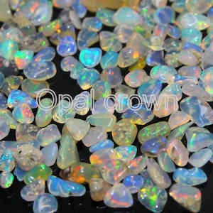 Könnte beinhalten: Eine Ansammlung kleiner, getrommelter Opal-Edelsteine mit durchscheinenden weißen, blauen und grünen Farbtönen und irisierenden Farbblitzen. Die Steine sind auf einer dunklen Oberfläche verstreut, der Text Opal crown steht in der Mitte in Weiß.