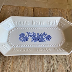 May include: A white rectangular serving dish with a blue floral design and the text "A joyous heart makes the loaves taste better".