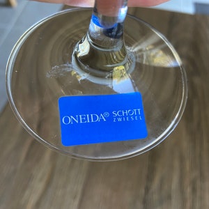 May include: A clear glass wine glass with a blue sticker on the bottom that reads "ONEIDA&reg; SCHOTT ZWIESEL"