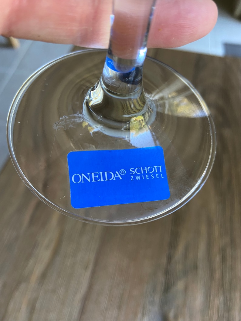 May include: A clear glass wine glass with a blue sticker on the bottom that reads "ONEIDA&reg; SCHOTT ZWIESEL"
