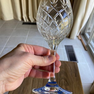 May include: A clear crystal wine glass with a cut diamond pattern. The glass has a blue band around the base.
