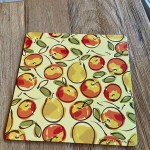 May include: A yellow placemat with a repeating pattern of red and yellow apples and pears. The placemat has a white background and the text "Hallmark Licensing, Inc." in the bottom right corner.