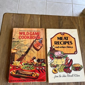May include: Two vintage cookbooks, one titled "Wild Game Cookbook" with a hunting scene and the other titled "Meat Recipes and Other Things" with a colorful illustration of food.