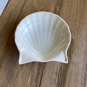 May include: A white ceramic seashell-shaped dish. The dish is smooth and has a glossy finish.