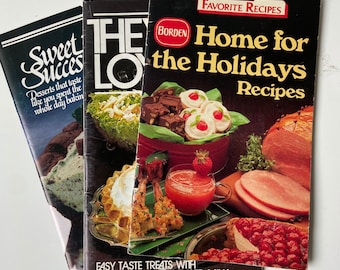 May include: Three vintage cookbooks with black covers and colorful food photography. The top book is titled "Home for the Holidays Recipes" with a red and white Borden logo. The middle book is titled "They Love" and the bottom book is titled "Sweet Success" with a green and white ice cream scoop on the cover.