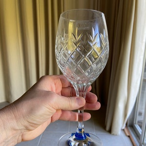 May include: A clear crystal wine glass with a diamond pattern. The glass has a blue sticker on the base.