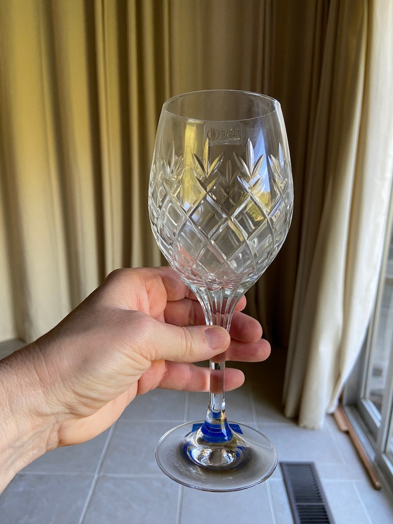 May include: A clear crystal wine glass with a diamond pattern. The glass has a blue sticker on the base.