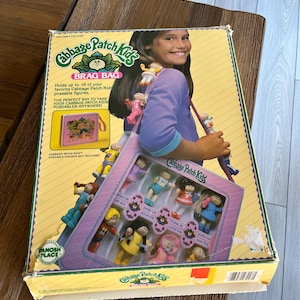 May include: Vintage Cabbage Patch Kids Brag Bag box. The box is yellow with a picture of a girl holding a bag with Cabbage Patch Kids figures. The box holds up to 16 poseable figures. The text on the box reads "Cabbage Patch Kids".