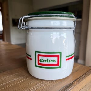 May include: White glass jar with a green lid and a red and green stripe design. The jar has a metal latch and the word "etcetera" printed on the front.