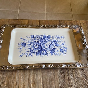 May include: A silver serving tray with a white base and a blue floral design. The tray has a decorative border with a floral pattern.