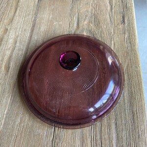 May include: A purple glass lid with a textured surface and a small purple knob in the center.