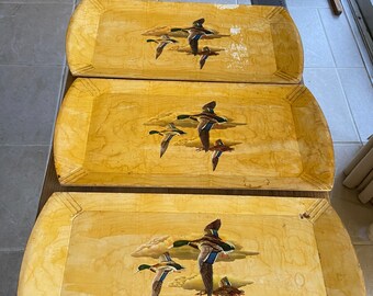 May include: Three wooden trays with a yellow background and a painted design of ducks flying in the sky. The trays are stacked on top of each other.