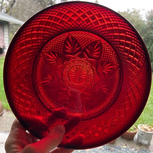 May include: A deep red glass plate with a starburst pattern in the center and a diamond pattern around the edge.