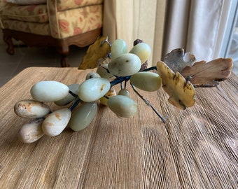 May include: A carved jade grapevine with green and brown leaves. The grapes are a light green color and are arranged in a cluster.