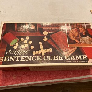 May include: A vintage Scrabble brand Sentence Cube Game box with a brown background and a picture of two people playing the game. The box has the text "Sentence Cube Game" and "1971 Selchow & Righter Co."